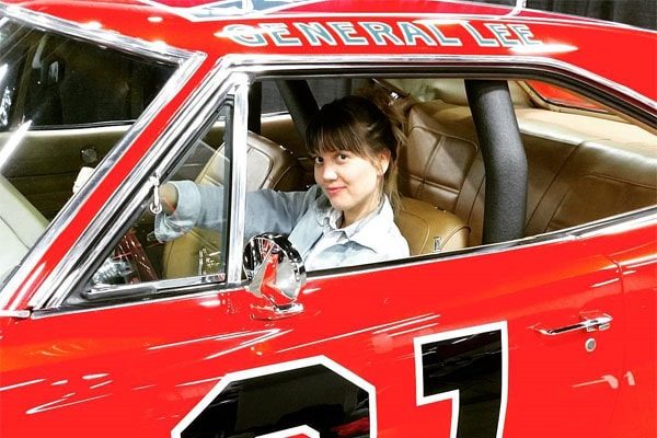 Nicki Clyne in a red luxury sports car.